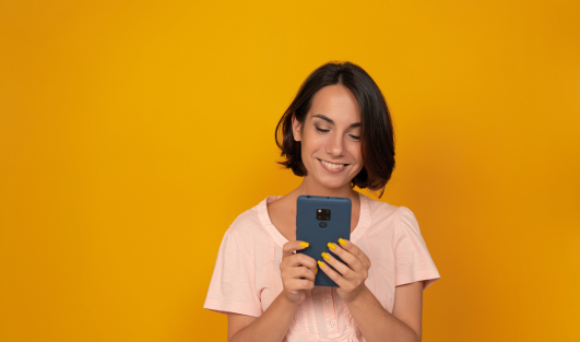 A woman holding a phone with both hands and looking at it while smiling.