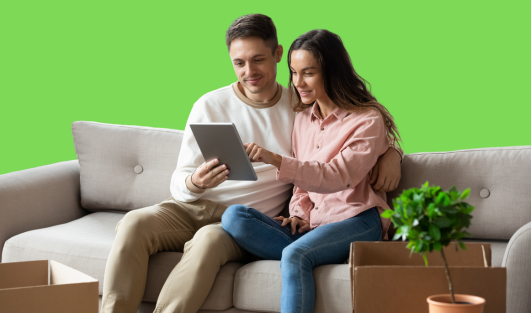 A man and woman sitting on a couch looking at a tablet together.