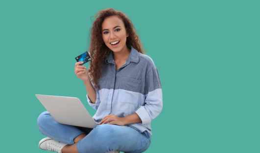 A woman sitting with a laptop on her lap and holding a card up while smiling.