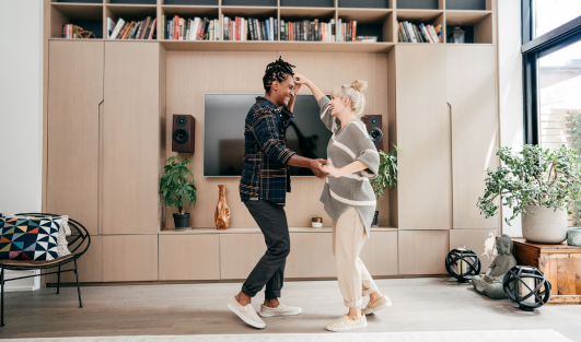 A man and woman holding hands and dancing in the living room of a house.