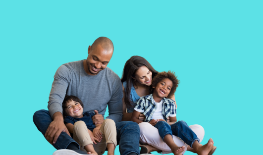 A man sitting with a child in his lap looking down at him smiling, and a woman sitting next to the man with another child in her lap looking at him smiling.