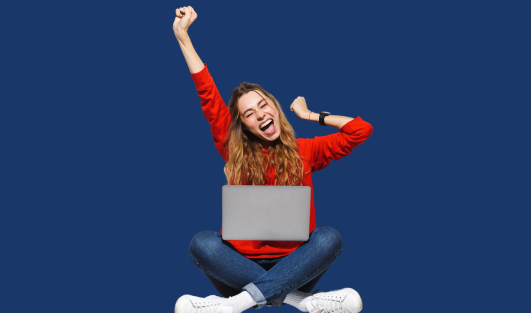 A woman smiles and excitedly puts her hands in the air while a laptop is sitting on her lap.