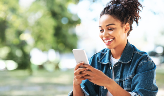 A woman smiling while looking at her phone that she's holding.