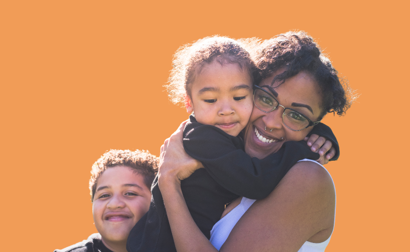 A woman hugging a little boy with another little boy close by smiling.