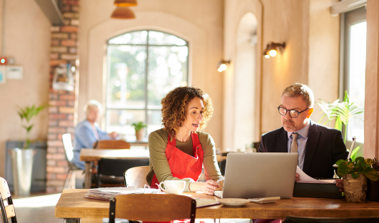 A woman sitting at a table with a professionally dressed man looking at a laptop together.