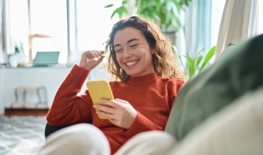 A woman smiling, sitting on a couch, looking at her phone.