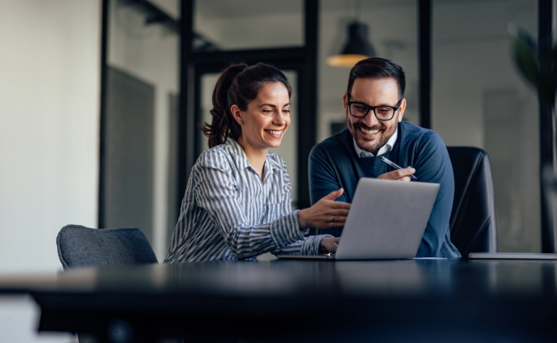 A woman and man in a professional setting looking at a laptop together.