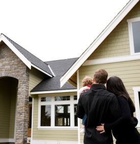 A man, woman, and child are facing a house, looking at it and embracing one another.