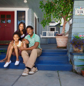 A man, woman, and child smiling while sitting on the front steps of a home.