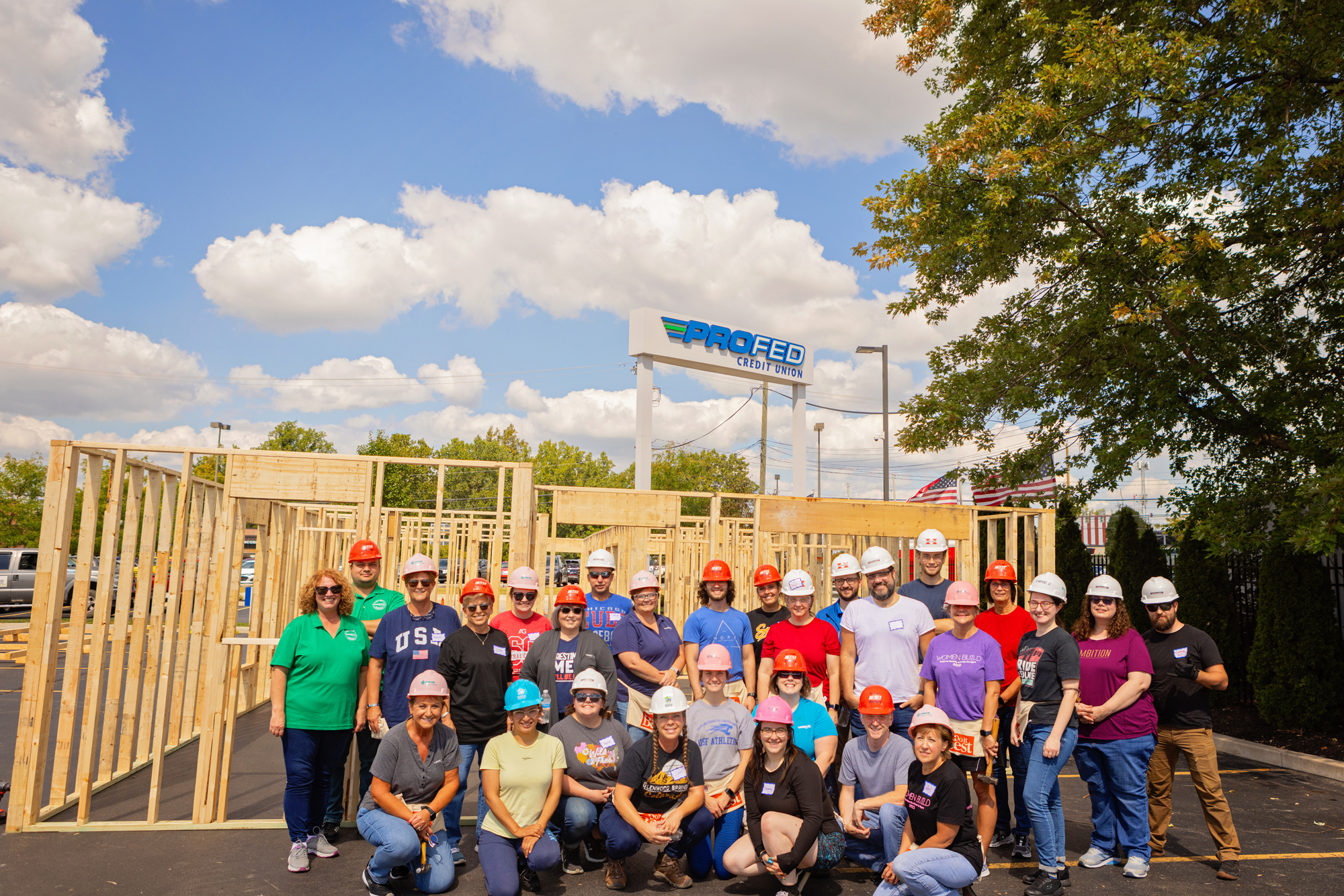 A group of ProFed employees with hard hats on after panel build day gathered together in front of framed-up walls.