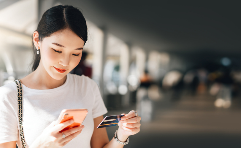 A woman looking at her phone while holding her credit card in her other hand.