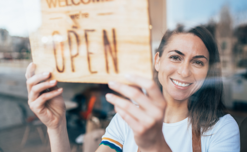 A woman holding an open sign inside a business.