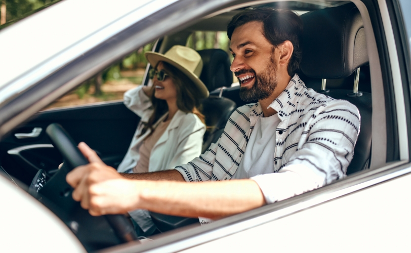 A man driving a car with a woman in the passenger seat wearing a hat and sunglasses.