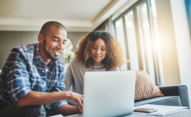 A man and woman looking at a laptop together in a home with the sun shining through the windows.