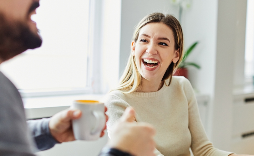 A woman smiling while looking at a man who is holding a mug in his hand.