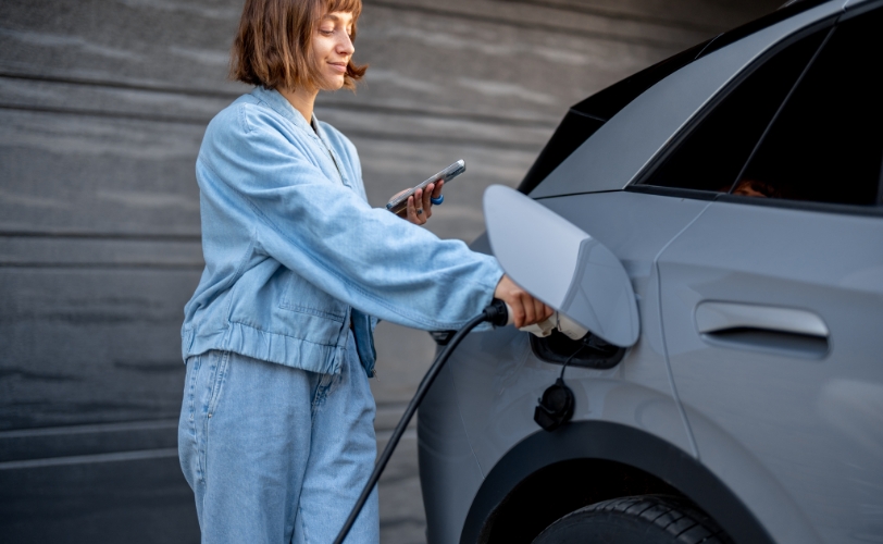 A woman pumping gas into her car while looking at her phone.