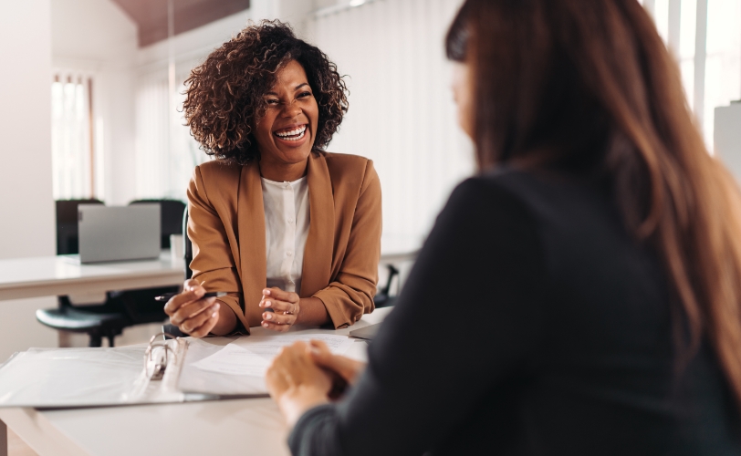 A woman smiling while meeting with another woman with documents on the table in between them.