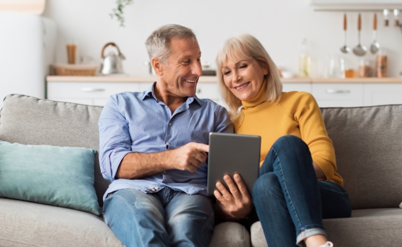 A man and woman sitting on a couch looking at a tablet together.