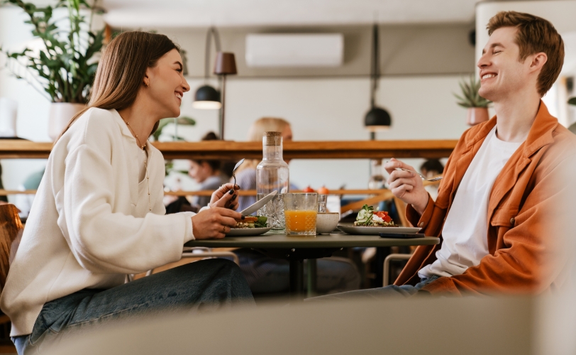 A woman and man sitting at a table inside a restaurant eating food.