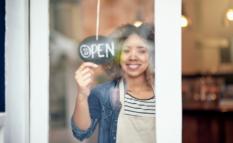 A woman holding an open sign in the door of a business.