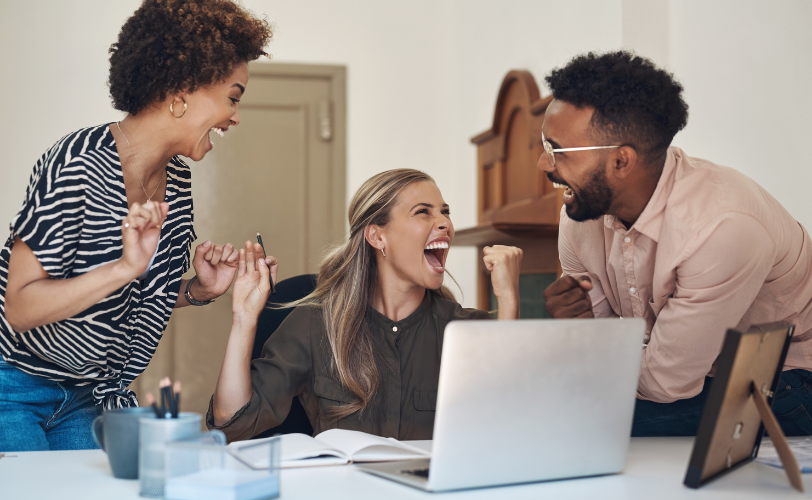 Two women and a man are celebrating something while in front of a laptop screen.