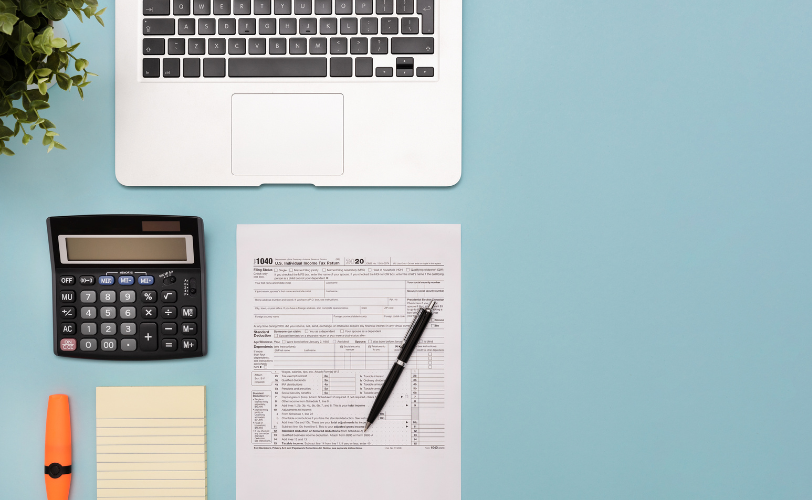 A laptop, calculator, pen, highlighter pad of paper, and document sitting on a table.