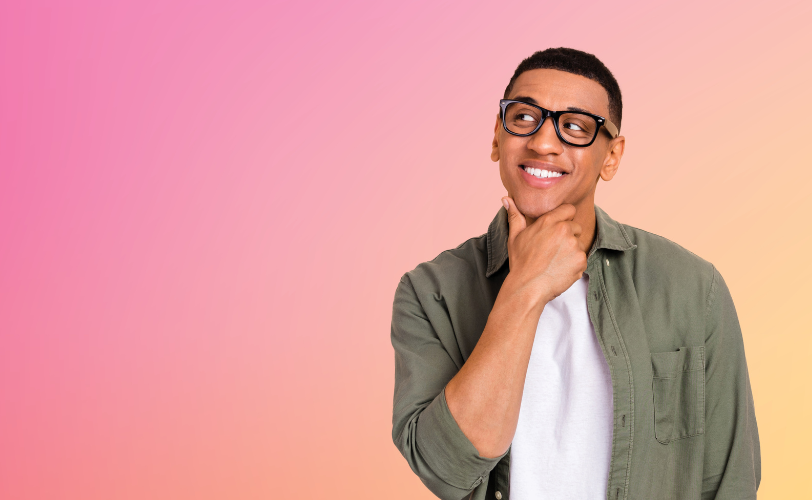 A young man smiles while looking off to the side with his hand on his chin like he's thinking.