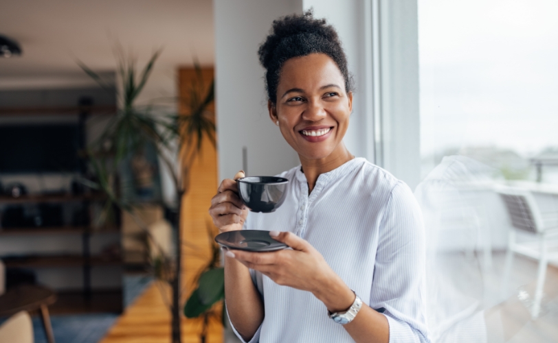 A woman smiling and holding a mug while looking out the window.