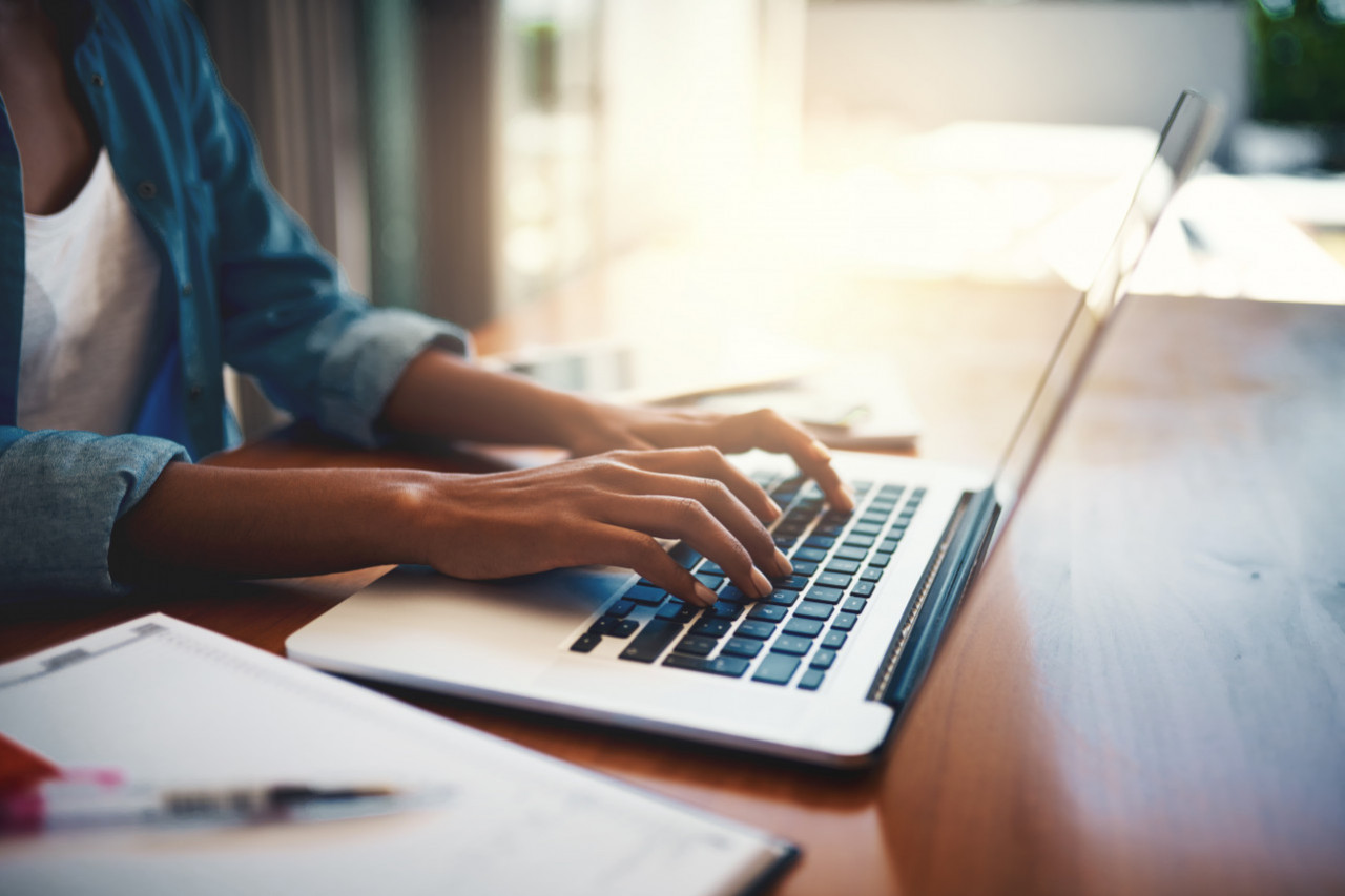 A woman at a desk and a laptop typing on the keyboard.
