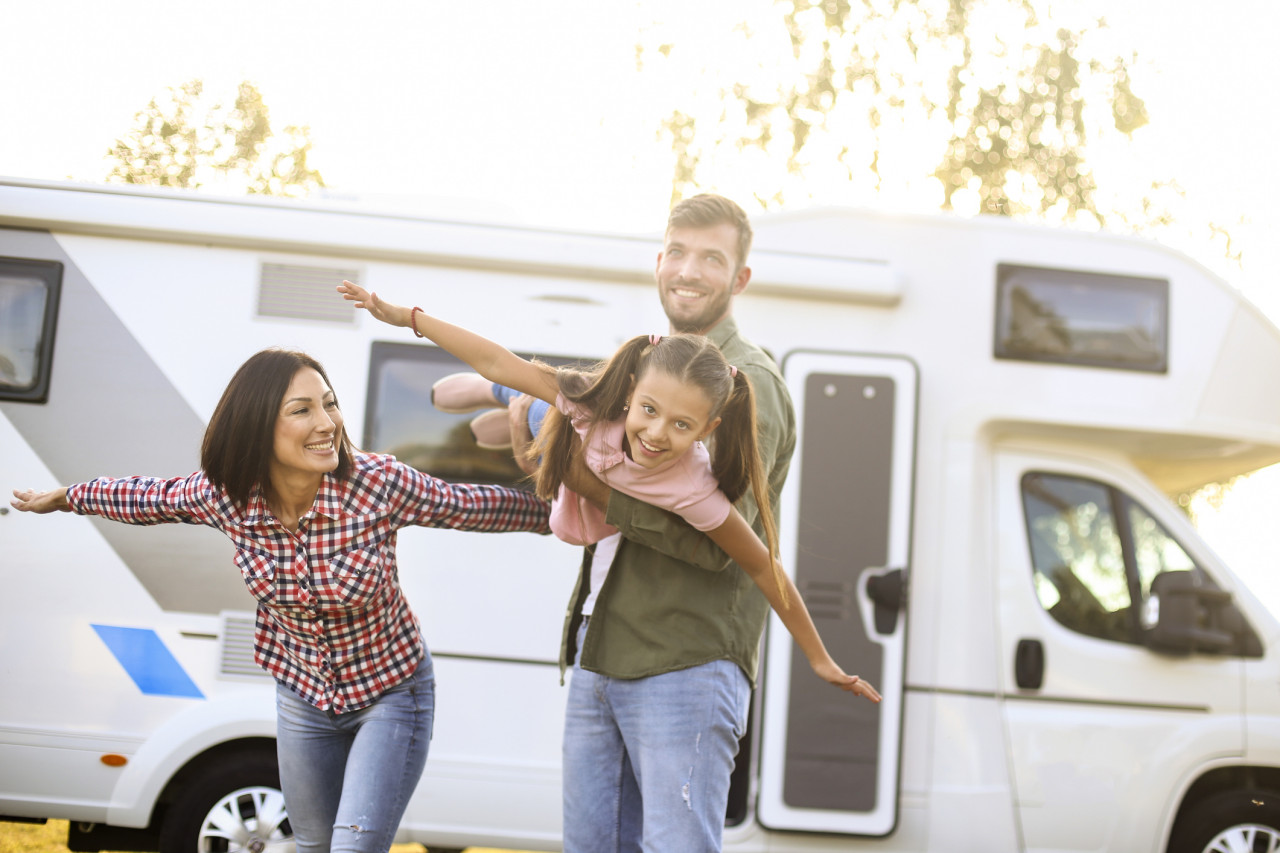A mom, dad and son pretending to fly like an airplane outside in front of their recreational vehicle.