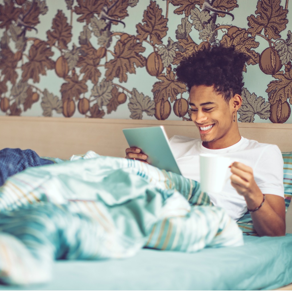 A young man laying in bed on his computer.