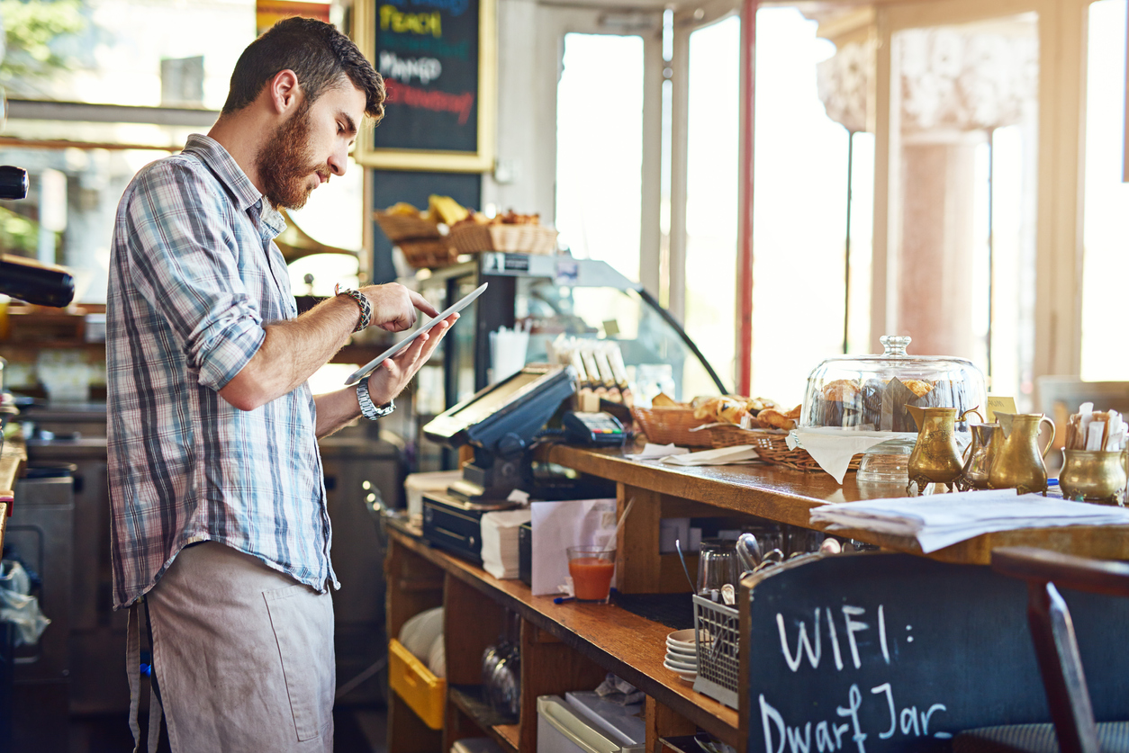 A man working behind the counter at a coffee shop on an ipad.
