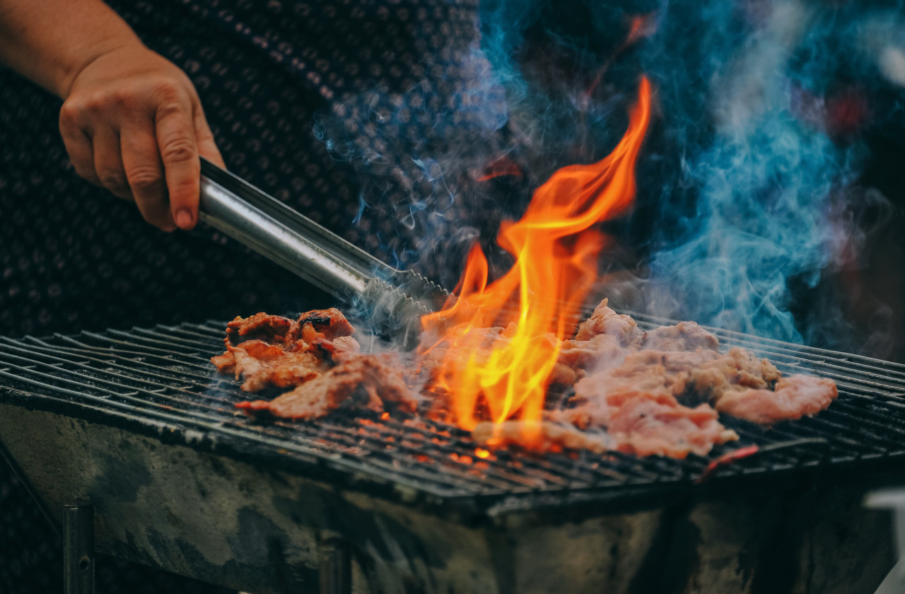 A man grilling meat with a big flame.