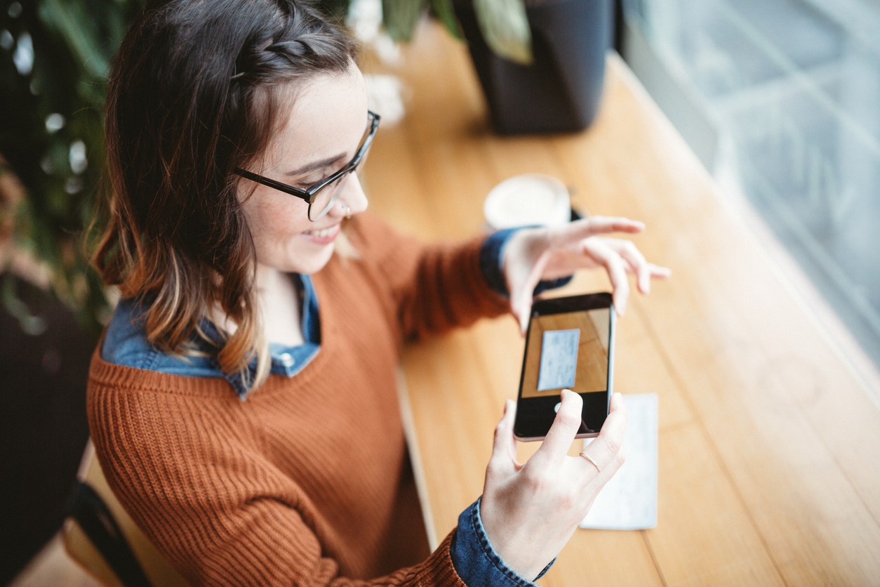A woman holding up her Iphone to snap a picture of her check to deposit it through her mobile app with ProFed.