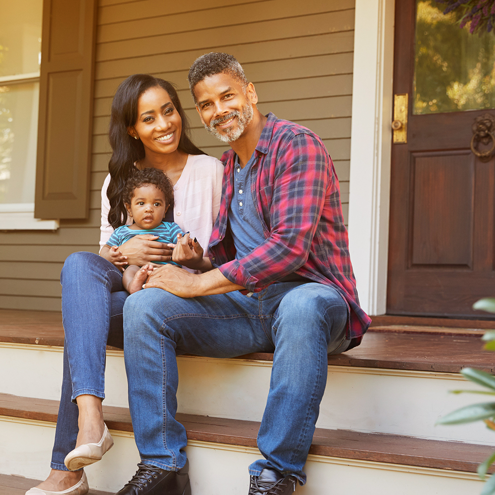 A couple and child sitting on their front steps on a sunny day.