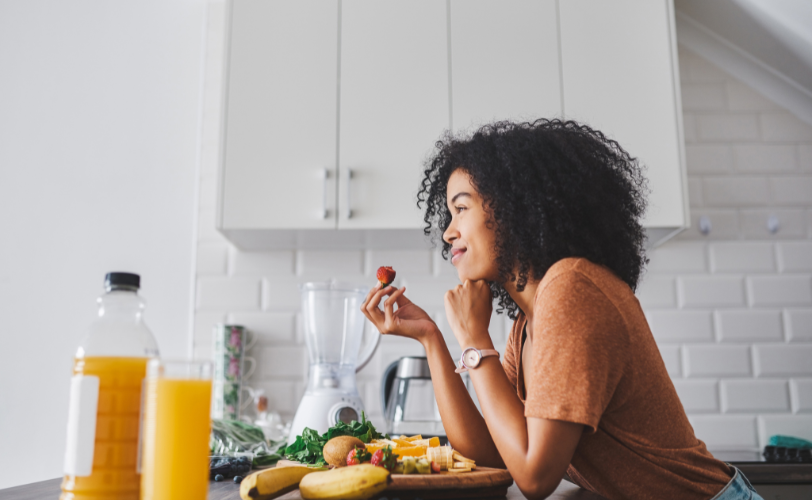 A woman eating breakfast at her counter while she smiles.