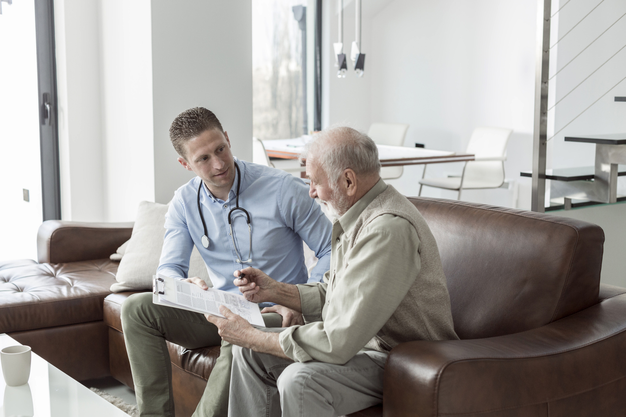 An older man sitting with a doctor on a couch filling out information on a sheet of paper.