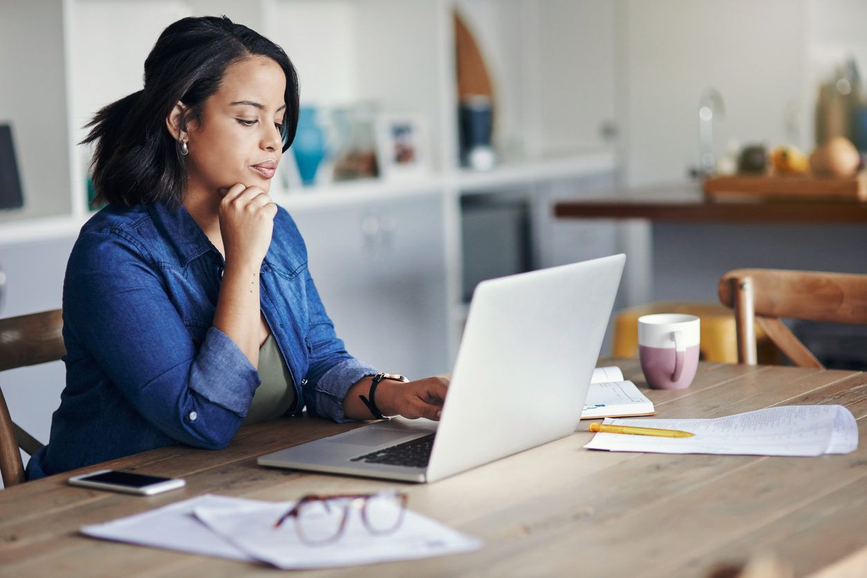 A woman sitting at a table in deep thought while looking at her laptop going over finanical information.