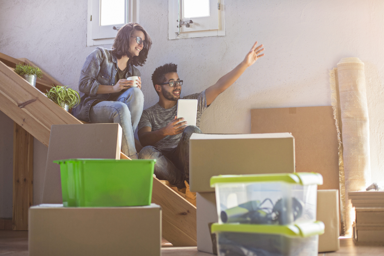 A couple smiling and disussing their future while sitting on the stairs of their new home they just moved into with boxes everywhere.