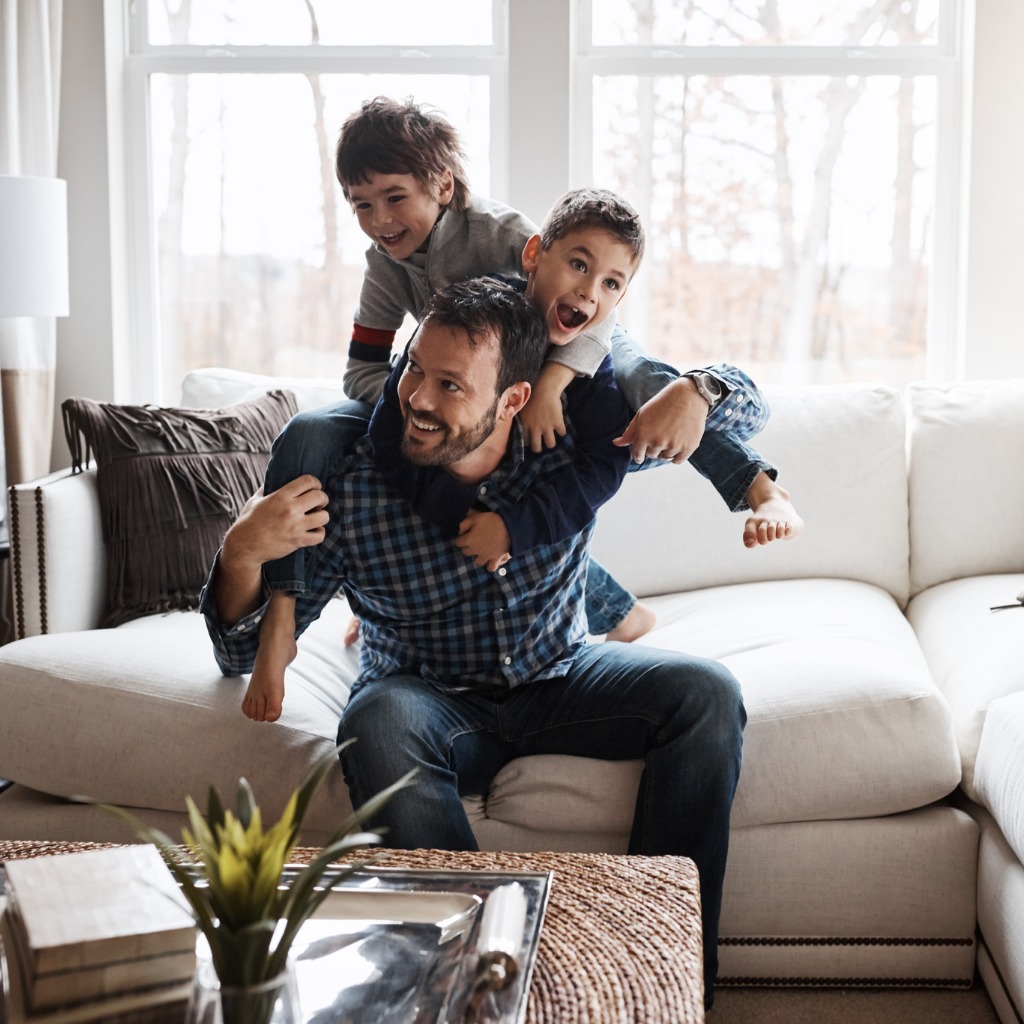 Father and two young boys play on their couch.