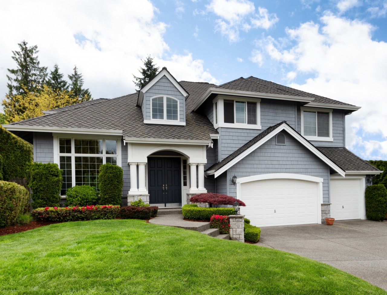 A large, modern two-story home with clean cut grass on a sunny day.