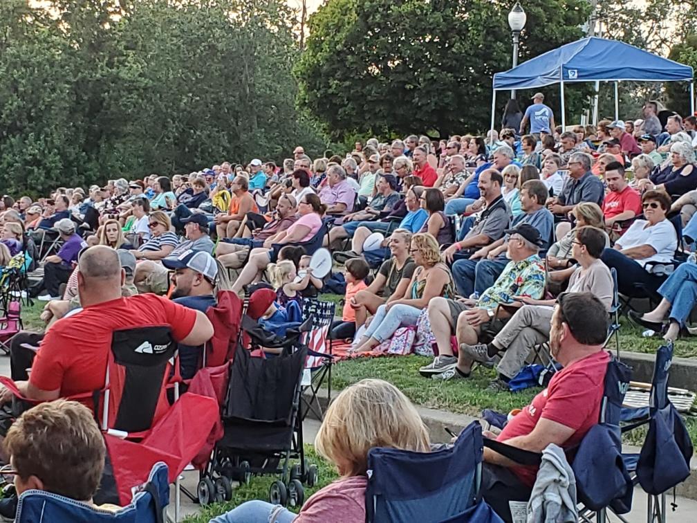 Crowd of people sitting on the lawn listening to music.