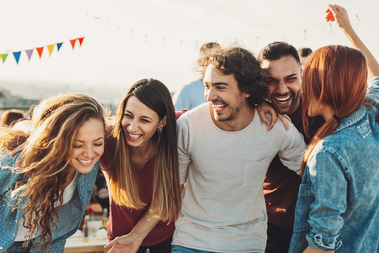 A group of friends laughing and embracing at an outside celebration.