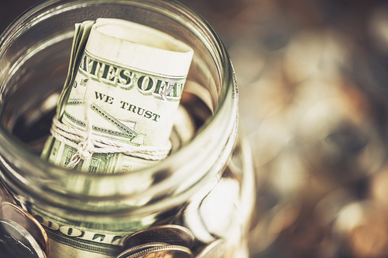 A glass jar of money filled with dollar bills and coins.