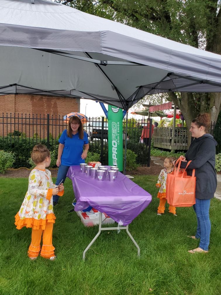 ProFed volunteer and little girls with their mom under a tent for the North Anthony Corridor Block Party.