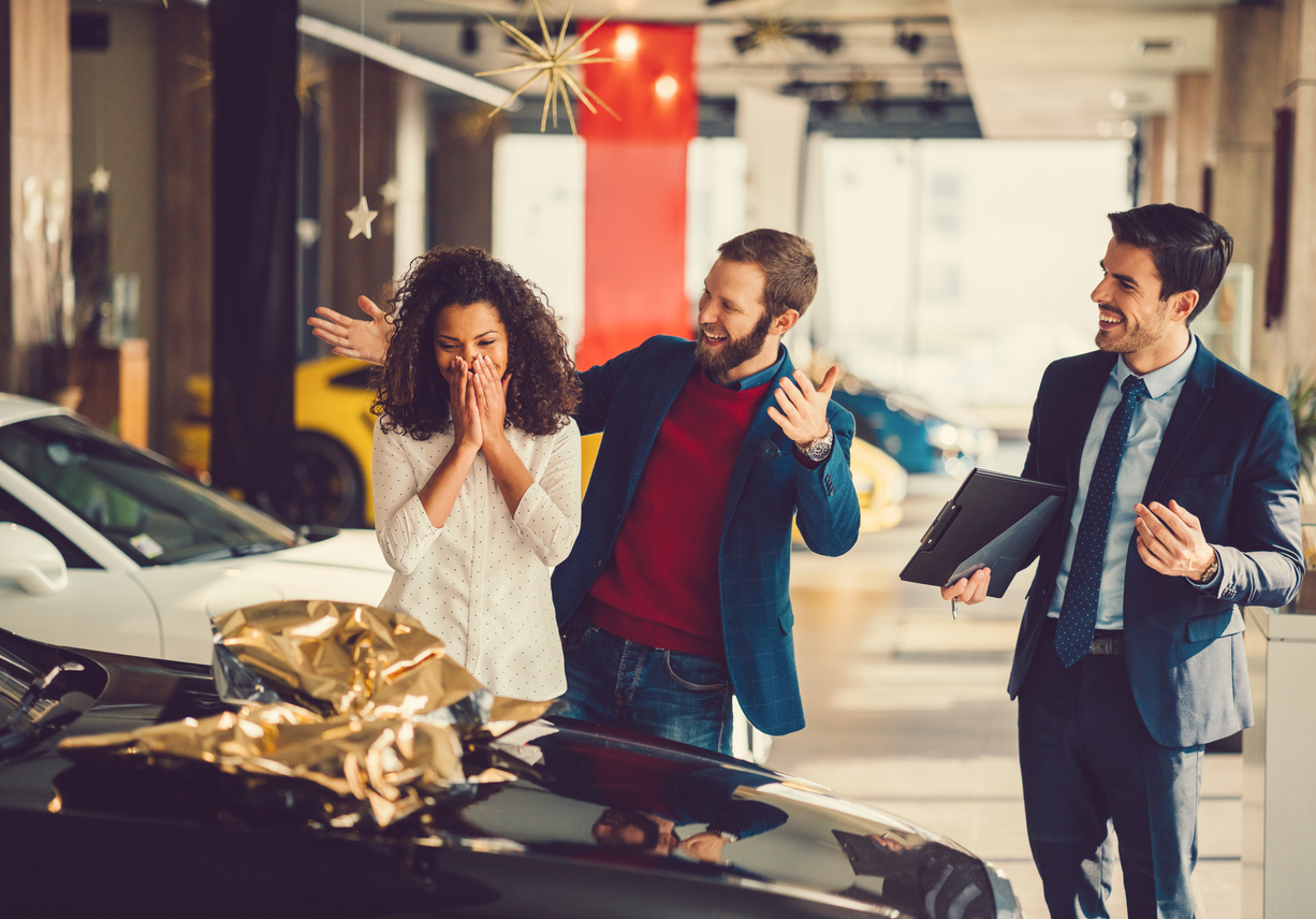 A man in celebration, surprising his wife with a brand new car.