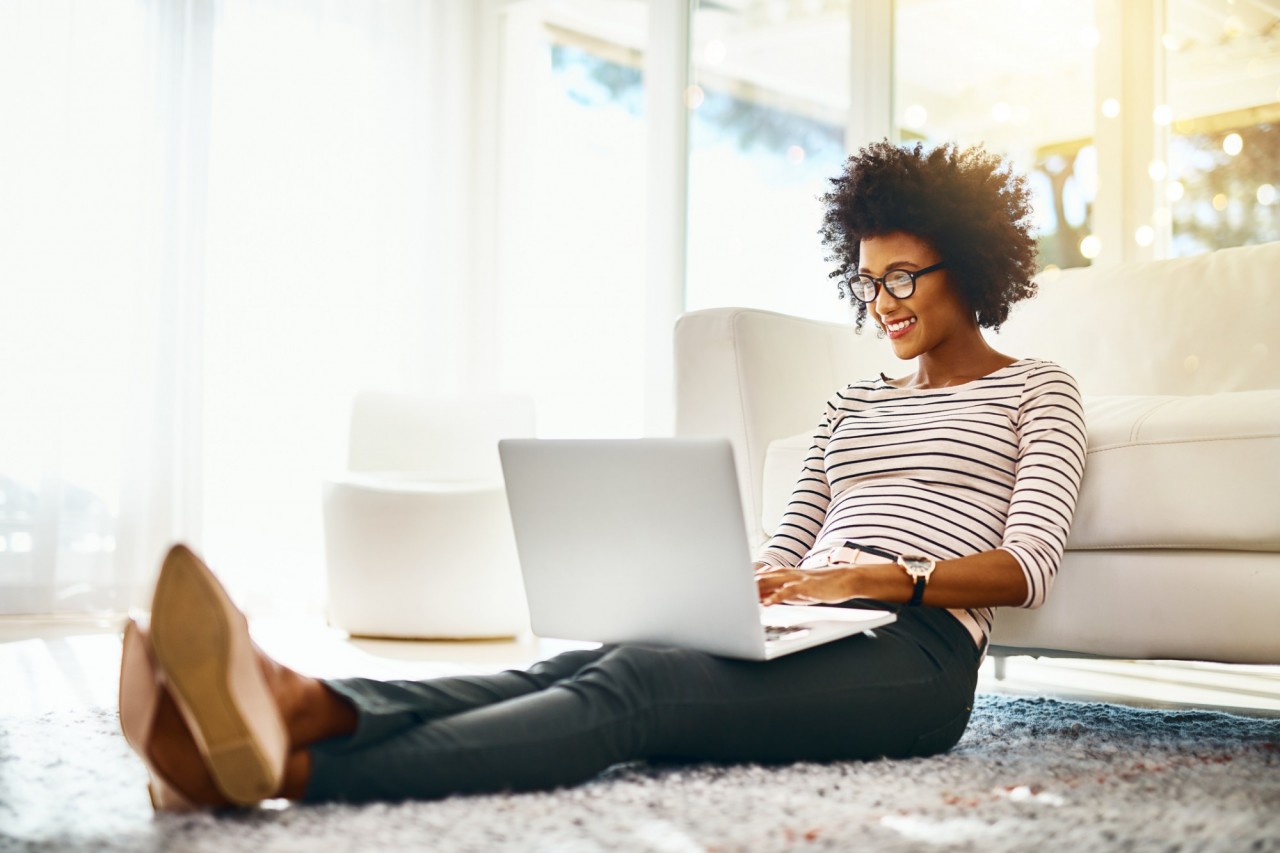 A woman with glasses sitting on the floor on her labtop.