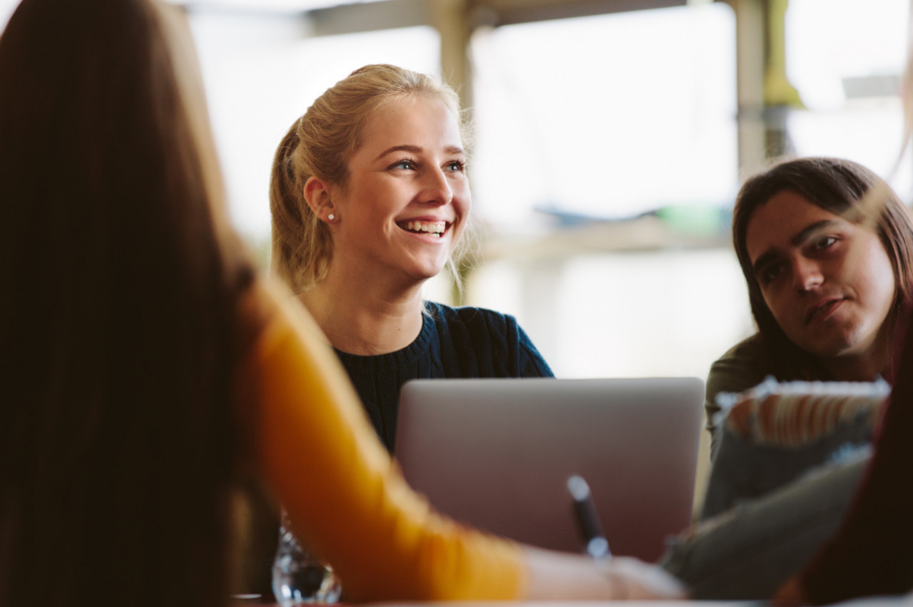 A student in a coffee shop on her laptop with a group of students.