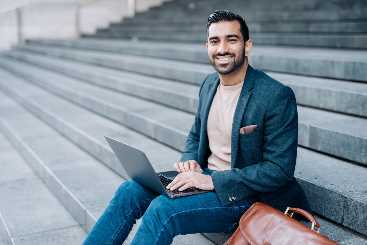 A man with a briefcase and laptop sitting outside on the steps of a professional building.