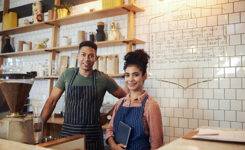 A business man and woman standing behind the counter of a coffee shop.